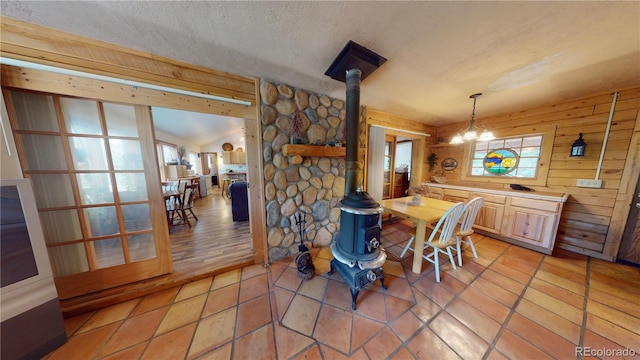 dining space featuring a notable chandelier, light tile patterned flooring, a wood stove, wooden walls, and a textured ceiling