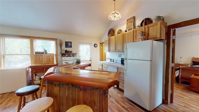 kitchen with decorative light fixtures, white fridge, sink, light hardwood / wood-style flooring, and lofted ceiling