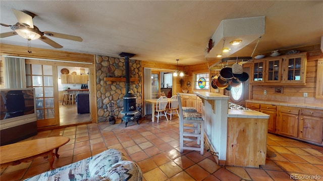 kitchen featuring a wood stove, tile counters, a breakfast bar, light tile patterned floors, and ceiling fan