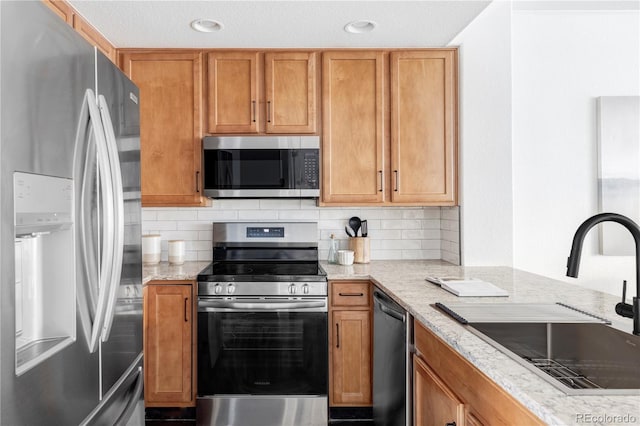 kitchen with light stone countertops, appliances with stainless steel finishes, sink, and backsplash