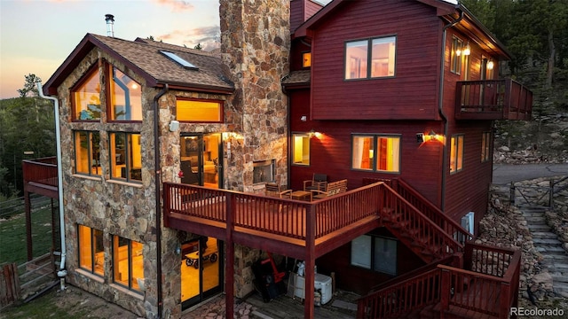 30717 Conifer Mountain Dr, Conifer, CO 80433 - back of house at dusk with stone siding, a balcony, a chimney, and a deck