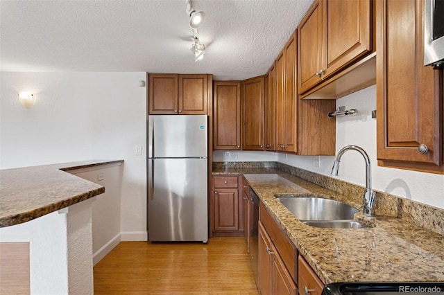 1 N Pearl St Unit 102, Denver, CO 80203 - kitchen with stainless steel appliances, a sink, brown cabinetry, light wood finished floors, and a textured ceiling