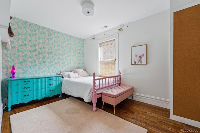 bedroom with wallpapered walls, an accent wall, wood finished floors, and baseboards