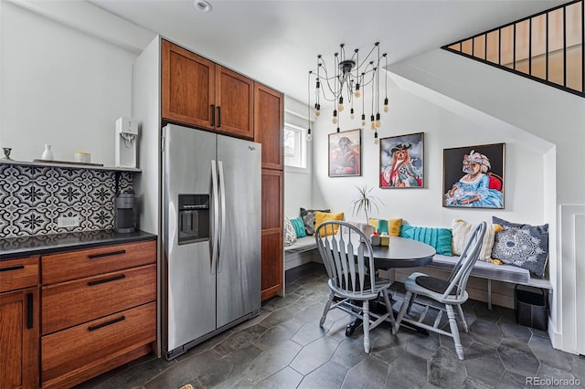 kitchen featuring stainless steel refrigerator with ice dispenser, breakfast area, dark countertops, brown cabinetry, and tasteful backsplash