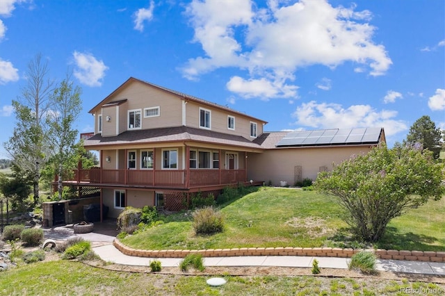 back of house featuring a deck, a lawn, roof mounted solar panels, a fire pit, and a patio