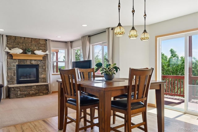 dining room featuring light wood finished floors, a stone fireplace, and recessed lighting