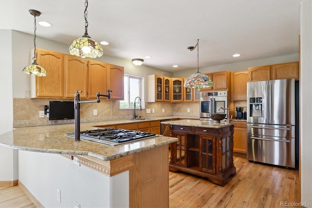 kitchen with appliances with stainless steel finishes, a sink, a peninsula, glass insert cabinets, and light wood-style flooring