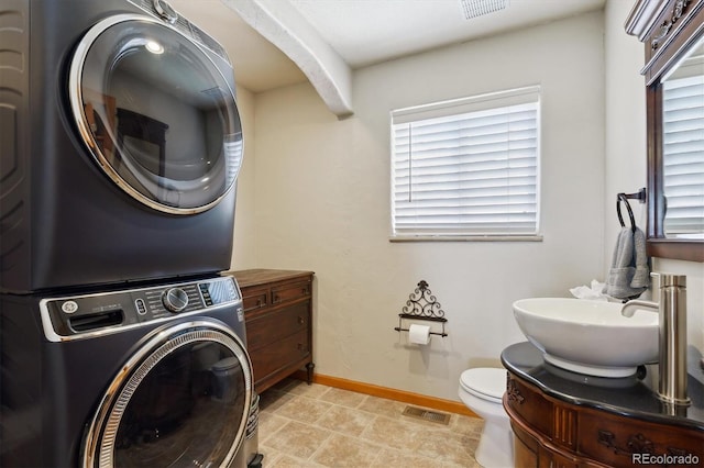 bathroom featuring stacked washer and clothes dryer, plenty of natural light, baseboards, and toilet