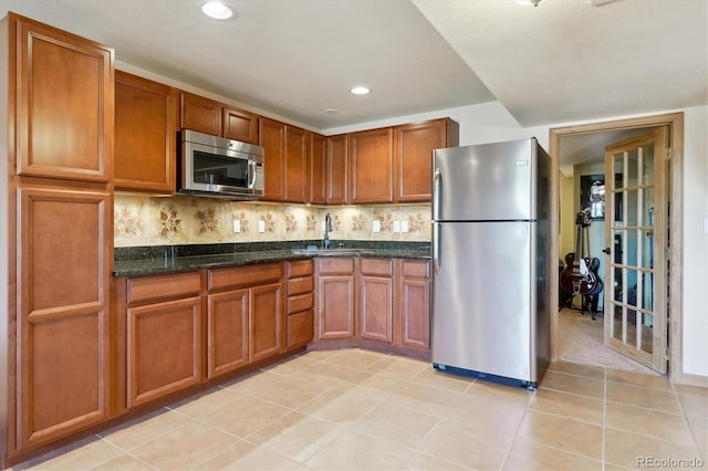kitchen with stainless steel appliances, a sink, brown cabinets, dark stone counters, and light tile patterned floors