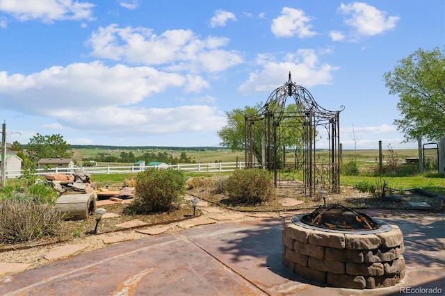 view of patio featuring an outdoor fire pit, fence, and a rural view