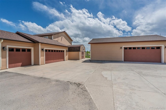 view of home's exterior featuring a garage, an outbuilding, roof with shingles, and driveway