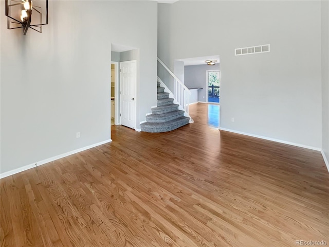 unfurnished living room with hardwood / wood-style floors, a chandelier, and a high ceiling