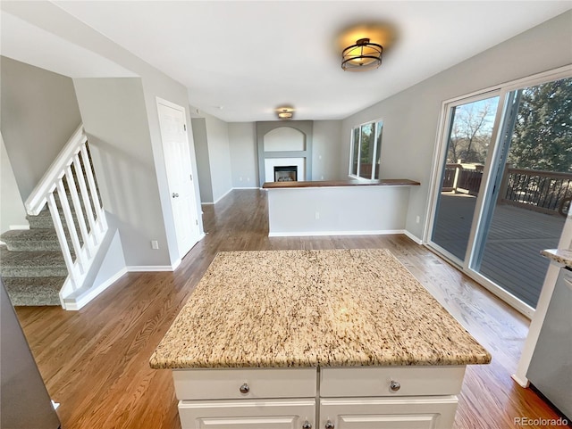 kitchen with white cabinetry, hardwood / wood-style floors, light stone counters, and a kitchen island