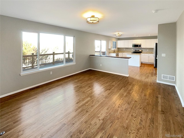 kitchen featuring hardwood / wood-style flooring, kitchen peninsula, white cabinets, and appliances with stainless steel finishes