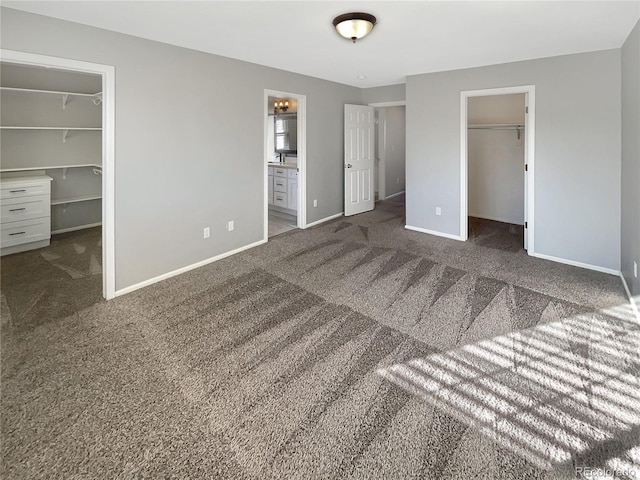 unfurnished bedroom featuring dark carpet, a spacious closet, a closet, and ensuite bathroom