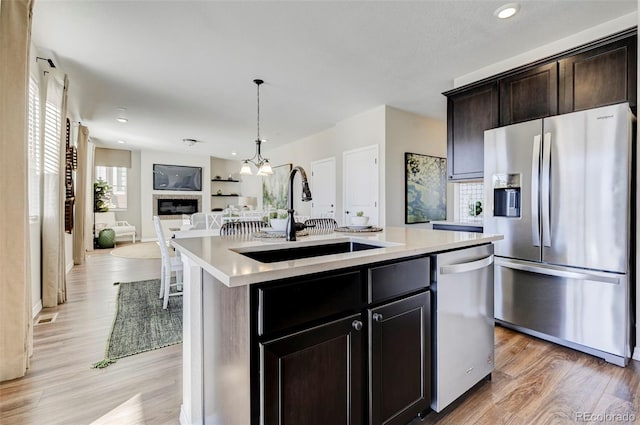 kitchen with sink, hanging light fixtures, a center island with sink, appliances with stainless steel finishes, and light wood-type flooring