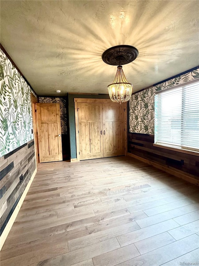 10704 Engelmann Ave, Salida, CO 81201 - unfurnished dining area with wallpapered walls, light wood-type flooring, a chandelier, a wainscoted wall, and wood walls