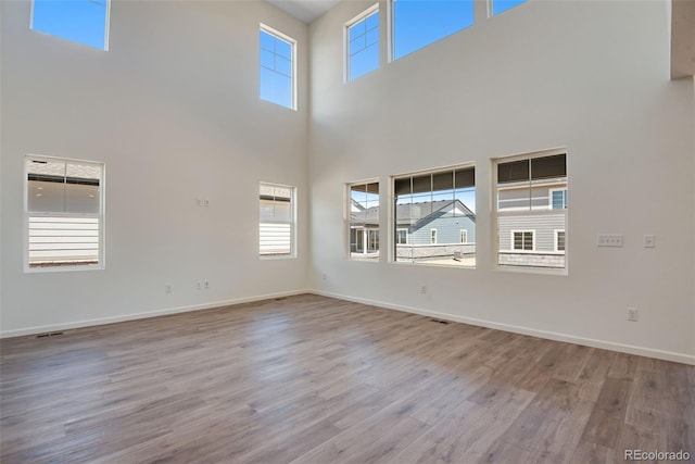 24563 E 34th Ave, Aurora, CO 80019 - unfurnished living room featuring wood finished floors, a towering ceiling, healthy amount of natural light, and baseboards