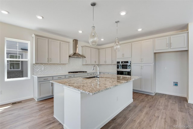 24563 E 34th Ave, Aurora, CO 80019 - kitchen featuring wall chimney range hood, light wood-style flooring, a center island with sink, backsplash, and recessed lighting