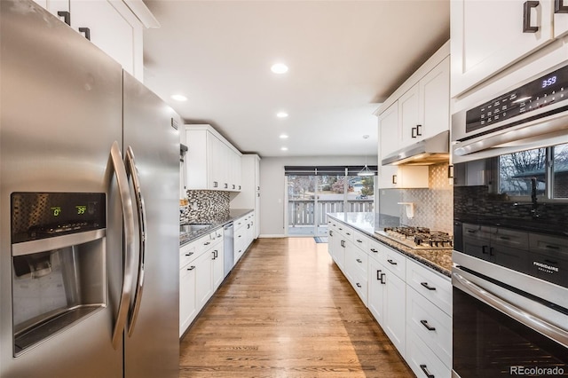 kitchen featuring dark stone counters, light hardwood / wood-style flooring, appliances with stainless steel finishes, tasteful backsplash, and white cabinetry