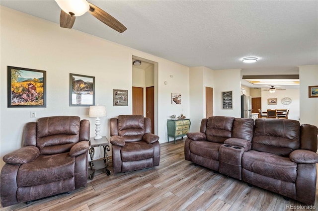 living room with ceiling fan, a textured ceiling, and light hardwood / wood-style flooring