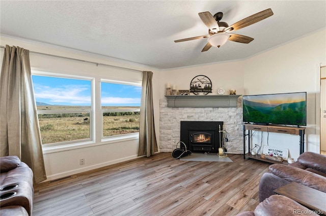 living room with a textured ceiling, light wood-type flooring, ceiling fan, and crown molding