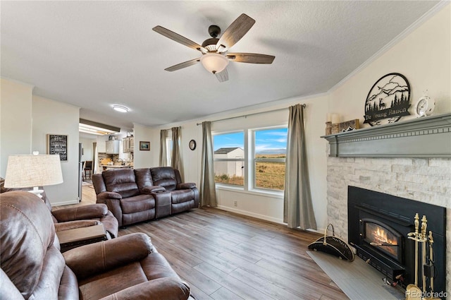 living room with a textured ceiling, ceiling fan, crown molding, a fireplace, and hardwood / wood-style floors