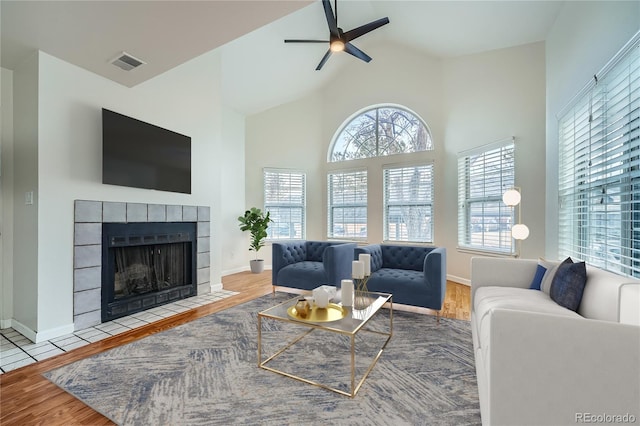 living room with a tiled fireplace, ceiling fan, wood-type flooring, and lofted ceiling