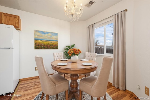 dining area with light wood-type flooring and a notable chandelier