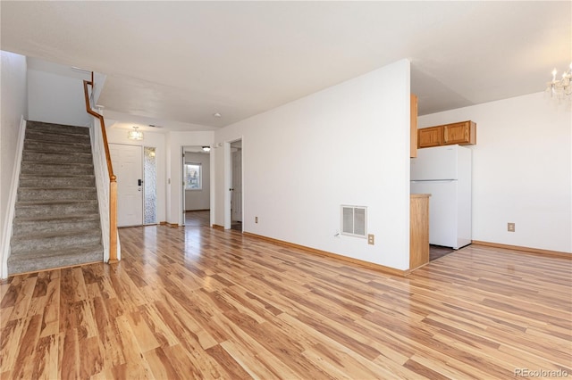 unfurnished living room featuring an inviting chandelier and light wood-type flooring