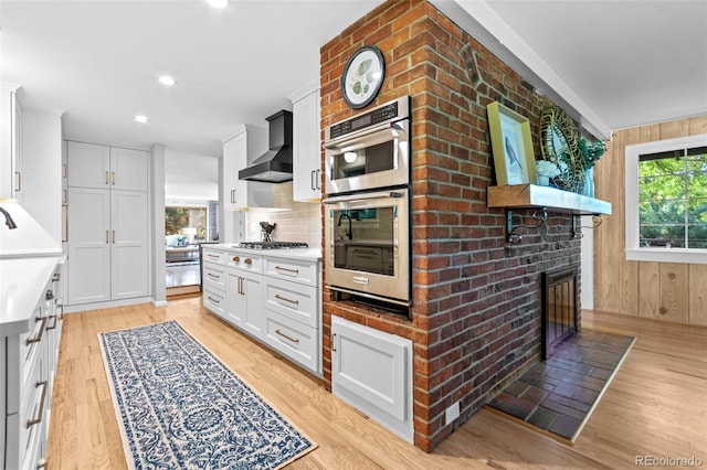 5465 W Ontario Ave, Littleton, CO 80128 - kitchen featuring wall chimney range hood, stainless steel appliances, light wood-style floors, decorative backsplash, and white cabinetry