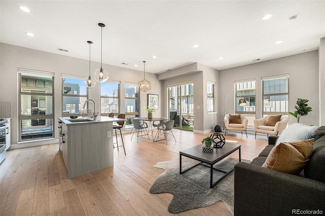 living room featuring sink, a wealth of natural light, a chandelier, and light wood-type flooring