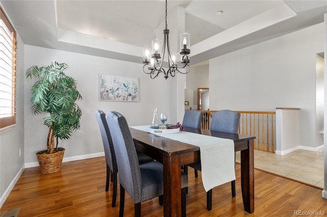 dining space with a tray ceiling, wood finished floors, visible vents, and an inviting chandelier