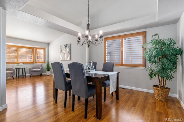 dining area featuring a raised ceiling, an inviting chandelier, vaulted ceiling, wood finished floors, and baseboards