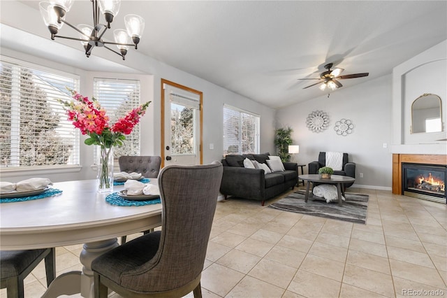 dining room with ceiling fan with notable chandelier, a glass covered fireplace, lofted ceiling, and light tile patterned floors