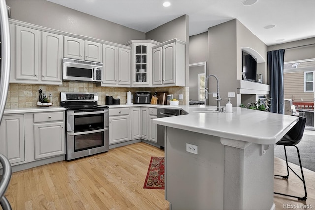 8378 Briar Trace Way, Castle Pines, CO 80108 - kitchen featuring appliances with stainless steel finishes, a kitchen bar, a peninsula, tasteful backsplash, and glass insert cabinets