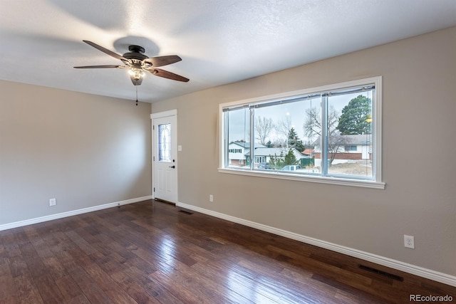 empty room with visible vents, baseboards, dark wood-type flooring, and a ceiling fan