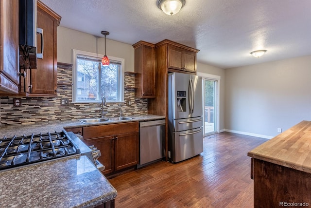 kitchen with dark wood-style flooring, a sink, decorative backsplash, stainless steel appliances, and dark countertops