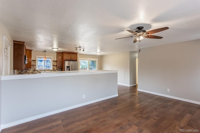 unfurnished living room featuring a textured ceiling, dark wood-style floors, baseboards, and ceiling fan