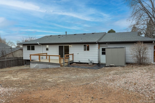 rear view of property featuring a shingled roof, a deck, and fence