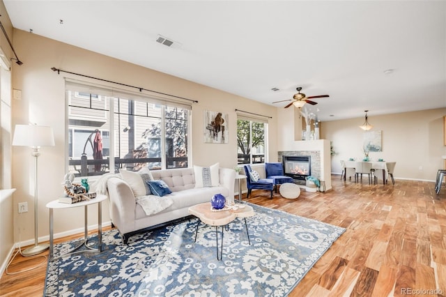 living area featuring wood finished floors, a fireplace, a ceiling fan, and baseboards