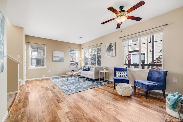 living area with light wood-style floors, a ceiling fan, and baseboards