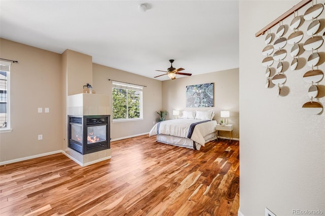 bedroom with light wood-style flooring, a multi sided fireplace, and baseboards