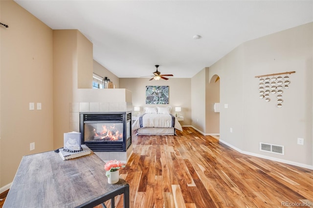 living area with light wood-type flooring, ceiling fan, a fireplace, and baseboards