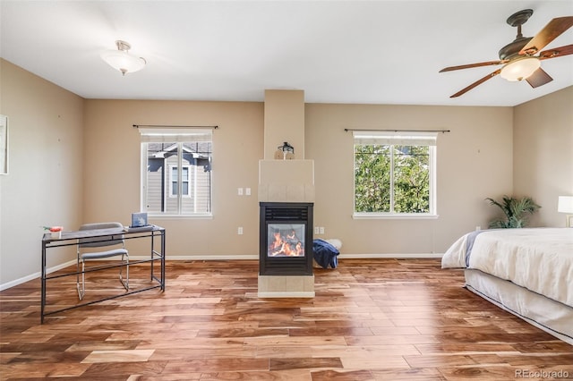 bedroom with wood finished floors, a tile fireplace, an office area, and baseboards