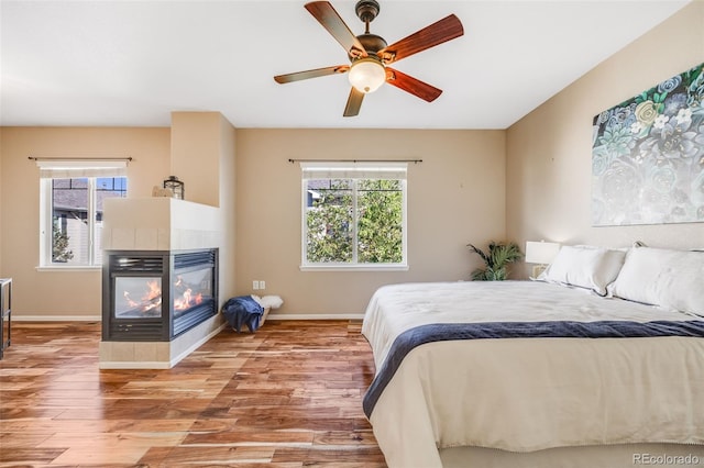 bedroom with wood finished floors, multiple windows, a tiled fireplace, and baseboards