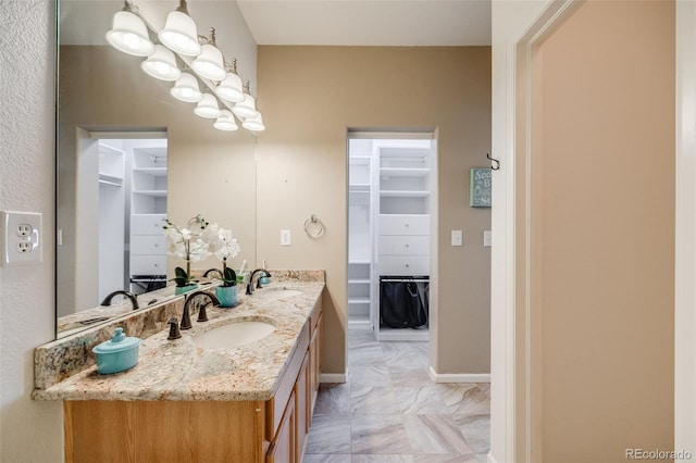 bathroom featuring a walk in closet, double vanity, and baseboards