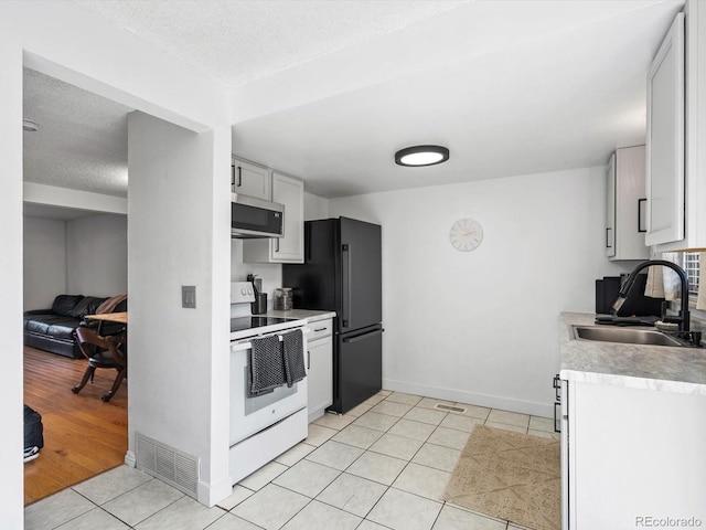 kitchen with freestanding refrigerator, white range with electric cooktop, visible vents, stainless steel microwave, and a sink