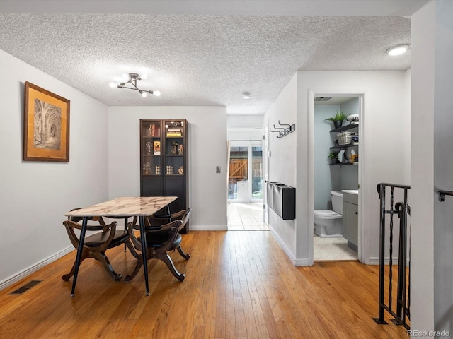 dining area featuring a textured ceiling, light wood finished floors, baseboards, and visible vents