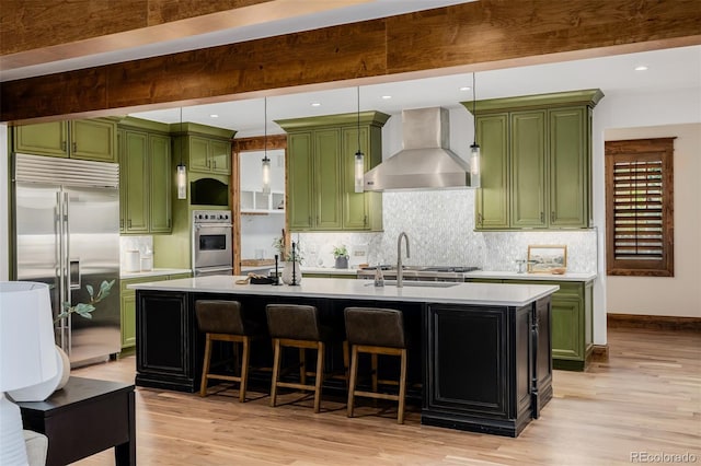 1332 S Lafayette St, Denver, CO 80210 - kitchen with green cabinets, stainless steel appliances, wall chimney range hood, light wood finished floors, and beamed ceiling